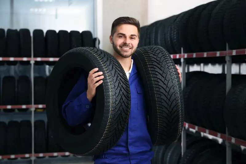 Male mechanic with car tires in auto store