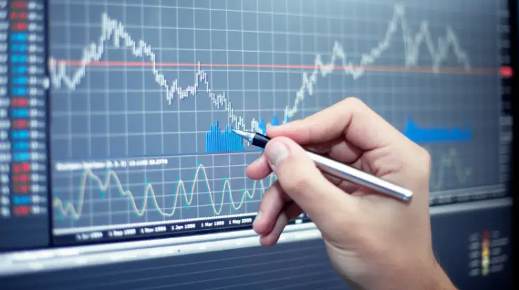 Hand of a person holding pen pointing to a trading graph