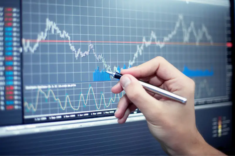 Hand of a person holding pen pointing to a trading graph