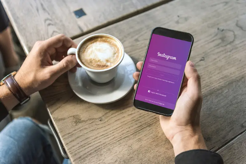 Cropped shot of man with cup of coffee using smartphone instagram apps on screen