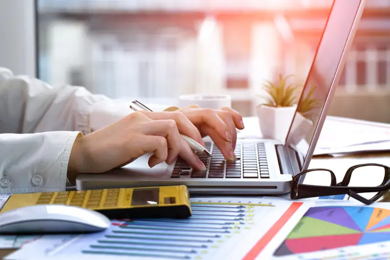 Woman working using laptop beside yellow calculator