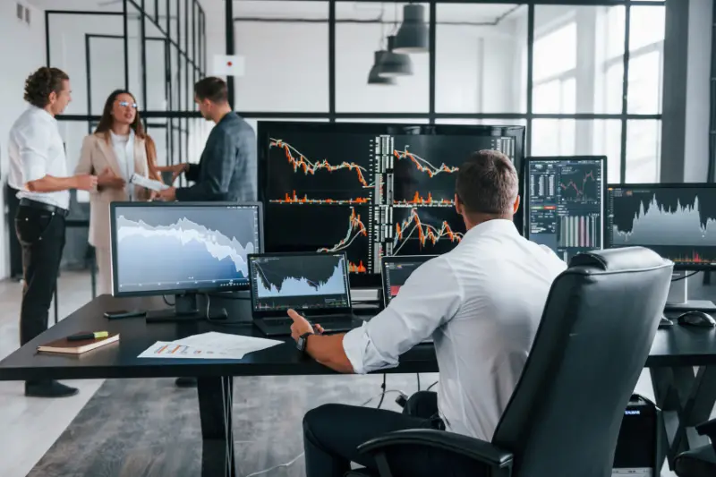 Team of stockbrokers works in indoors with many display screens