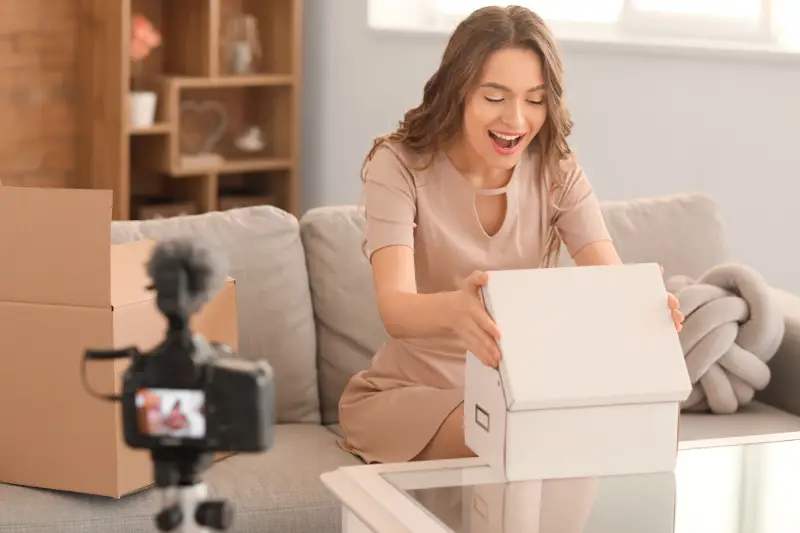 Young female blogger recording video while unpacking parcel at home