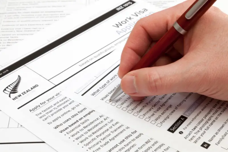 A man holding a ballpoint pen to fill a work visa application form to New Zealand