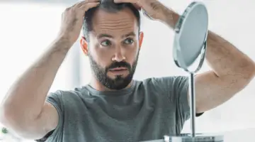 bearded mid adult man with alopecia looking at mirror, hair loss concept