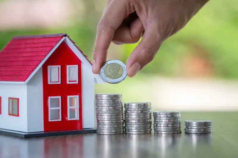 Hand putting money coin stack with small house