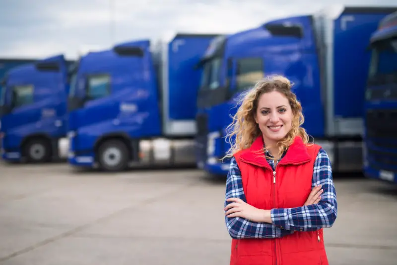Truck driver occupation. Portrait of woman truck driver in casual clothes standing in front of truck vehicles. Transportation service.