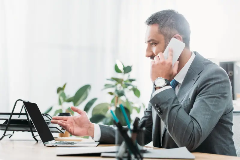 Businessman sitting in front of laptop and talking on smarphotne