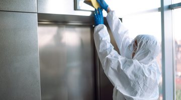 Cleaning and disinfection of the elevator to prevent COVID-19. Worker wearing protective suit sprays