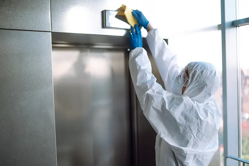 Cleaning and disinfection of the elevator to prevent COVID-19. Worker wearing protective suit sprays