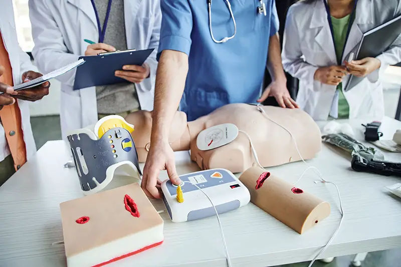 partial view of healthcare worker operating external defibrillator on CPR manikin