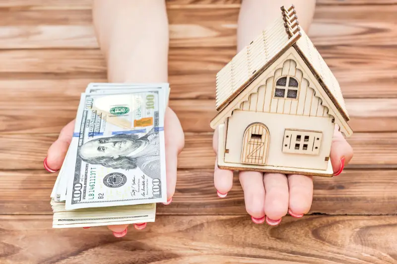 Woman's hands holding money and model of house over wooden table