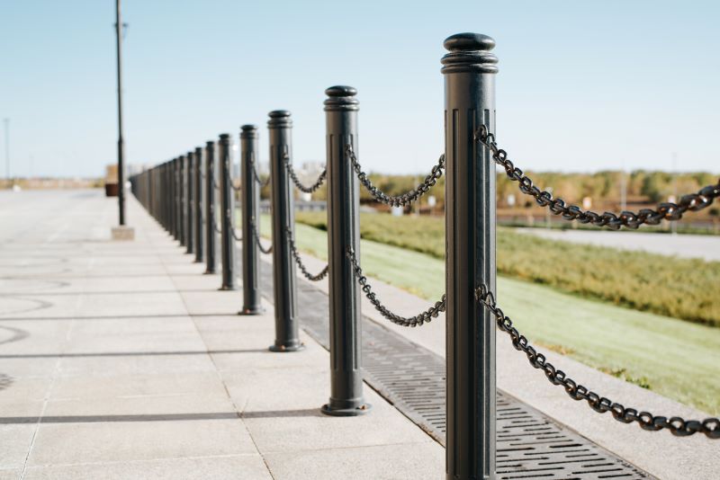 Black iron fence posts with chain. Decorative fence pillar outdoors on a sunny day, perspective view