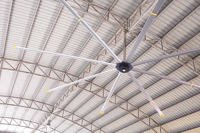 HVLS big fan on ceiling under the old metal curve roof structure of industrial building, low angle view with copy space