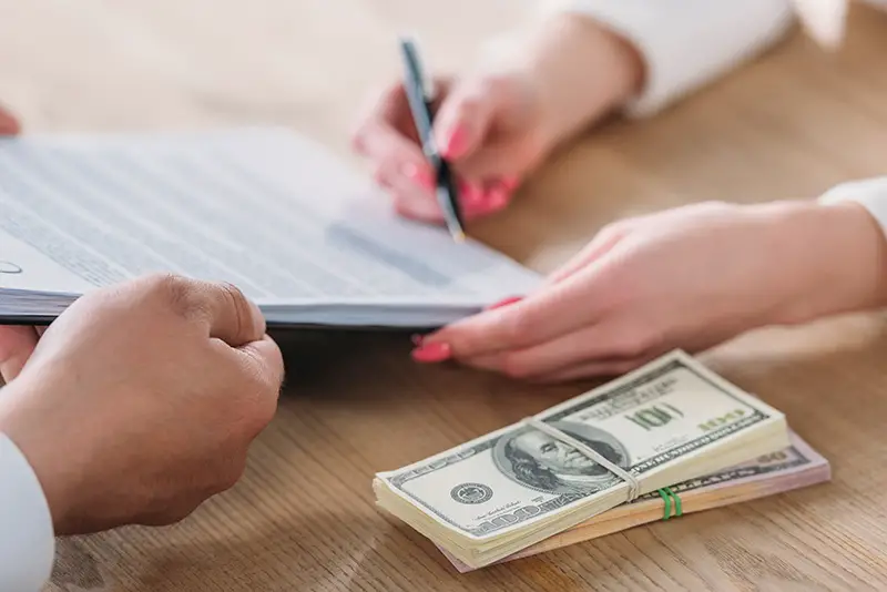cropped view of woman signing loan agreement on clipboard in hands of businessman near dollar