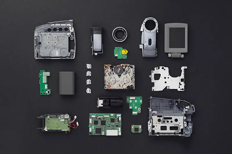 Parts of a mini DV video camera separate and well arranged over black background, above view.