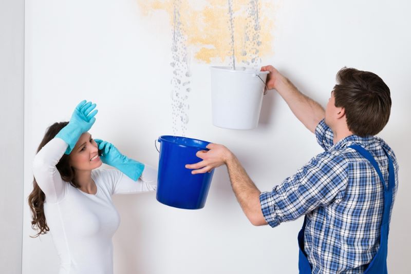 Young Woman Standing With Worker Collecting Water in bucket from ceiling wall