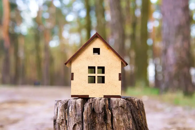 Close-up of a wooden toy house model placed on a tree stump in the forest