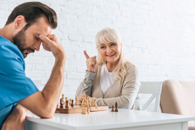 Smiling senior woman pointing with finger and looking at upset male carer