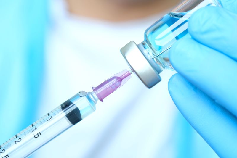 Doctor's hand holds a syringe and a blue vaccine bottle