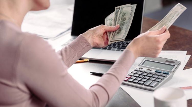 Cropped shot of woman counting money at table with laptop
