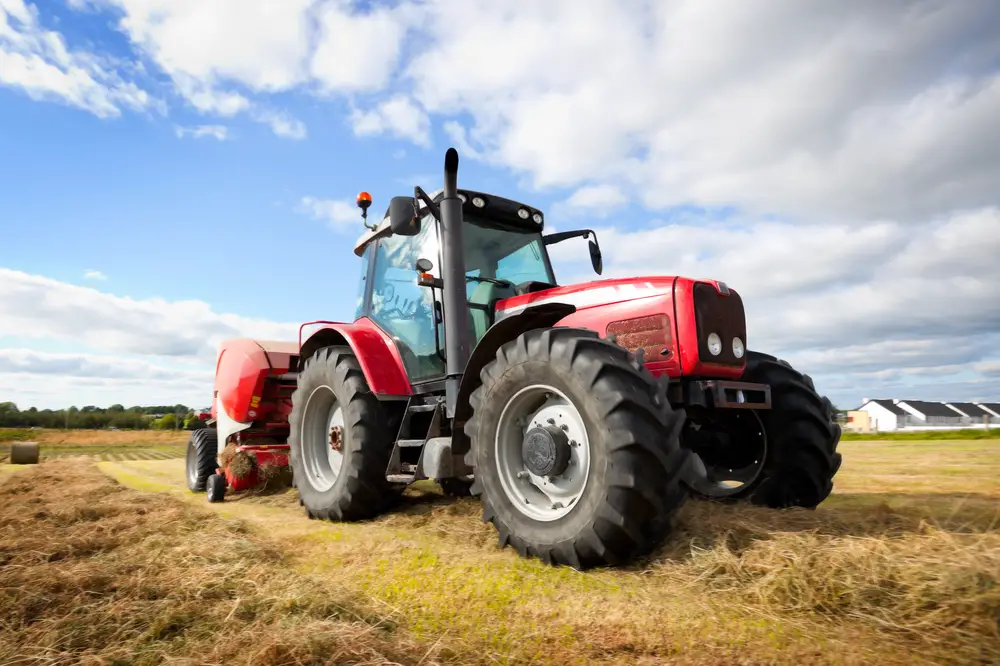 Red tractor collecting haystacks in the field