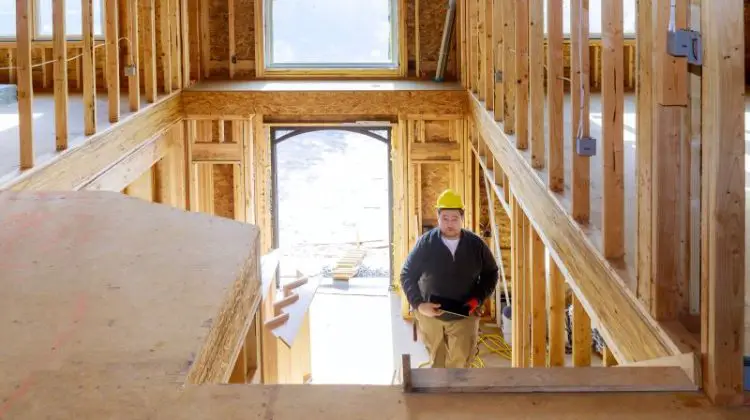 New construction house builder in hard hat walking up the stairs holding tablet PC