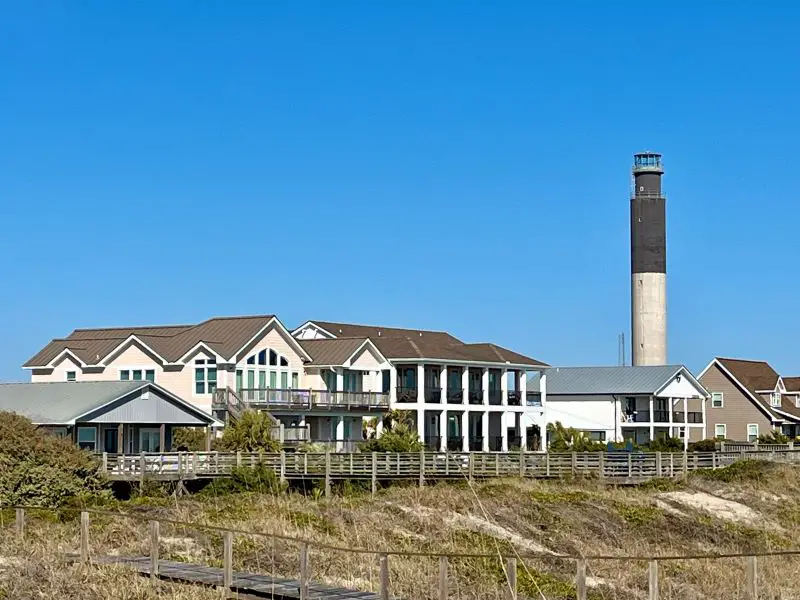 a lighthouse tower on the beach next to houses in a coastal region