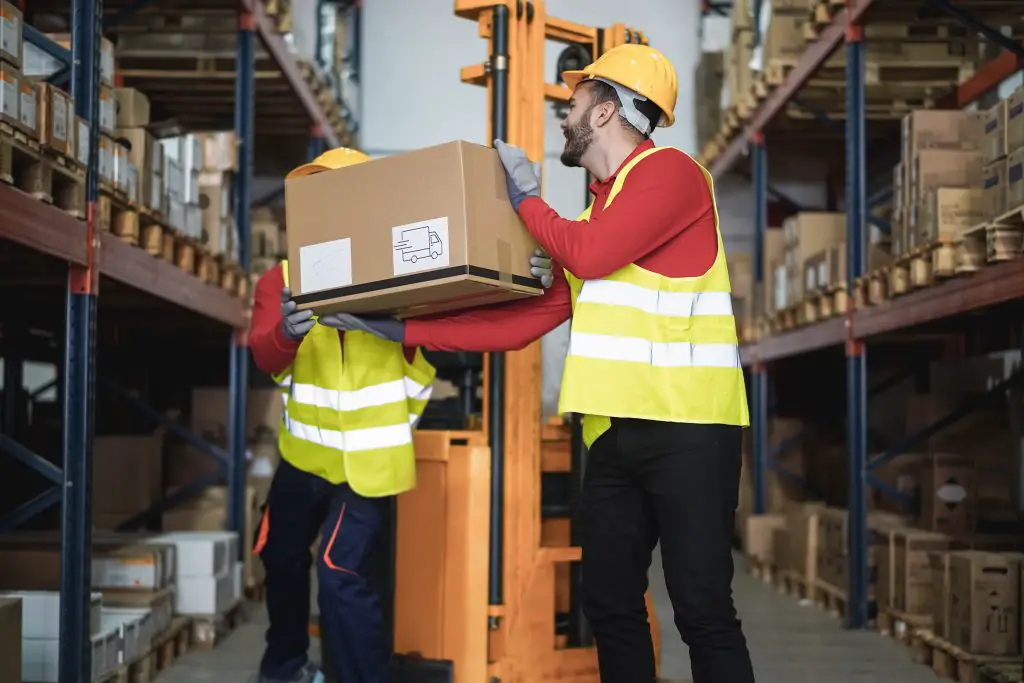 Industrial workers loading delivery box inside warehouse store - Focus on right man 