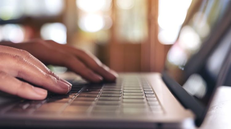 Closeup image of hands using and typing on laptop keyboard on the table on wooden table