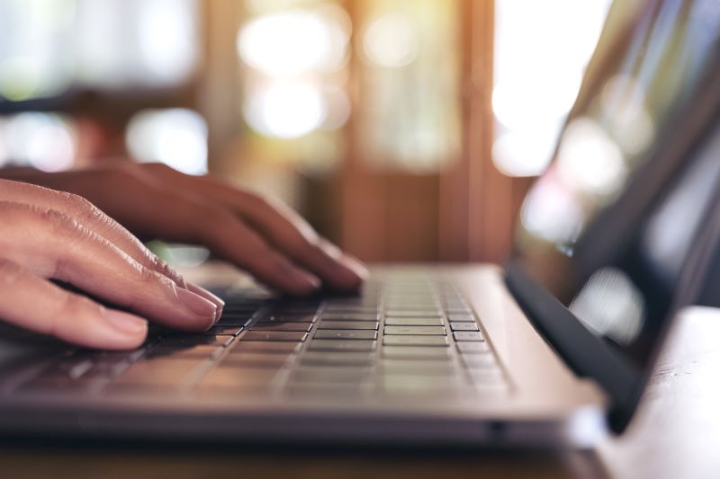 Closeup image of hands using and typing on laptop keyboard on the table on wooden table