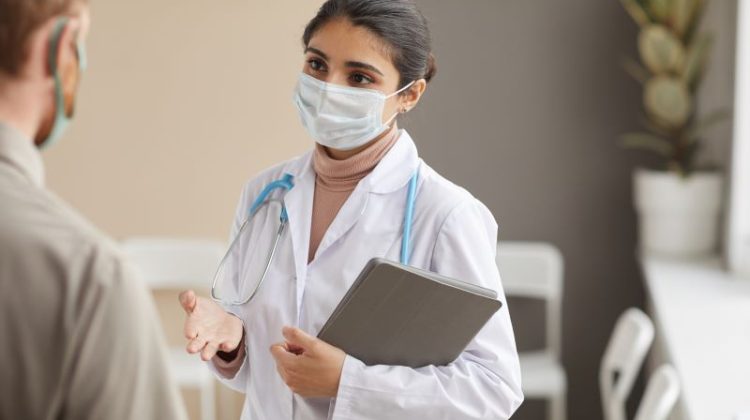 Young female doctor in protective mask talking to a patient