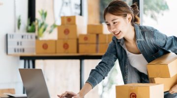 Asian woman entrepreneur is packing product to the box at home workplace.