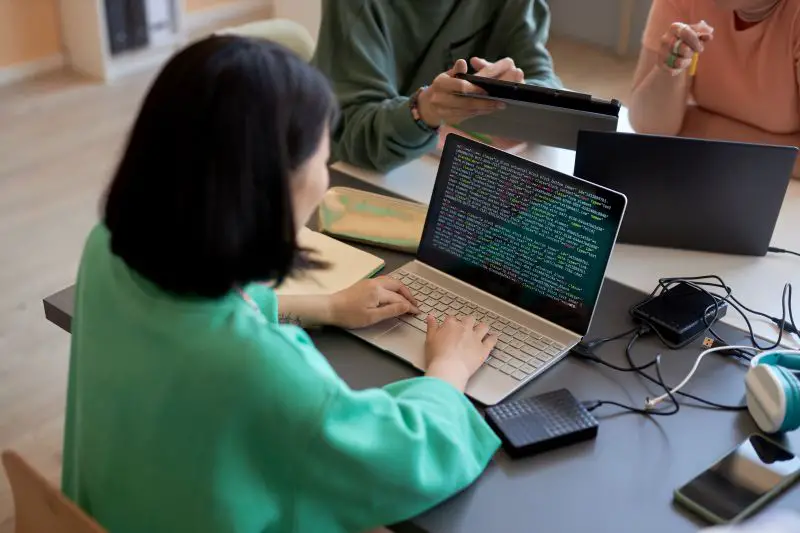 Young female student typing on laptop keyboard while decoding data