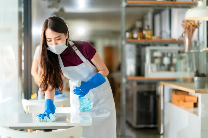 Asian staff waitress wearing protection face mask apron and rubber glove cleaning table