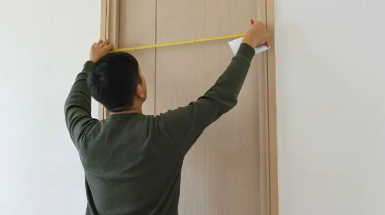 Man measuring a door size with a tape measure and holding a pen and paper.